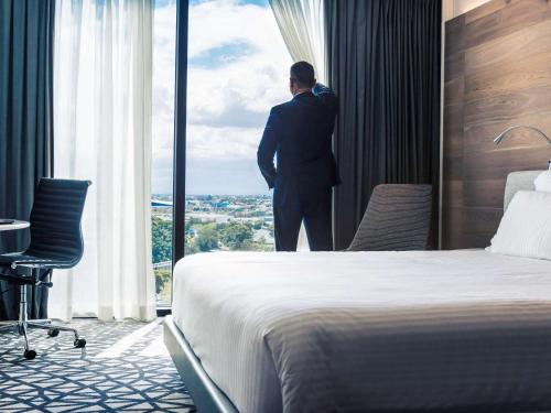 a man looking out the window of a hotel room at Pullman Sydney Airport in Sydney