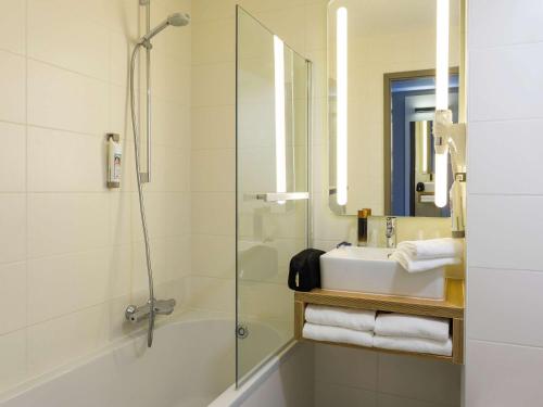 een badkamer met een douche, een wastafel en een spiegel bij ibis De Haan in De Haan