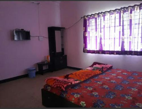 a bedroom with a bed with a red comforter and a window at Vamoose Laxmi Hill Resort in Satara