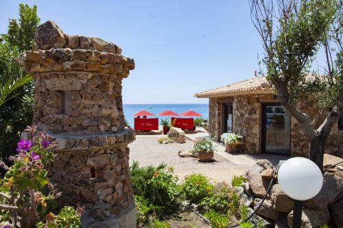 a stone house with a stone chimney in a garden at Hôtel et Résidence Ta Kladia - Omigna in Cargèse