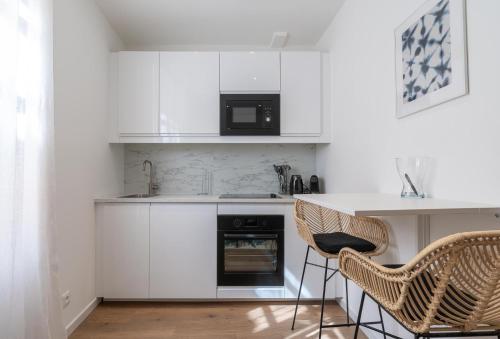 a kitchen with white cabinets and a counter and two chairs at Appartement PORTHALET in Saint-Tropez