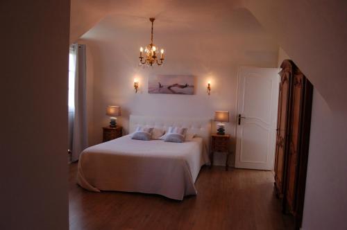 ein Schlafzimmer mit einem weißen Bett und einem Kronleuchter in der Unterkunft La Villa des Longchamps Location du samedi au samedi in Saint-Jouan-des-Guérets