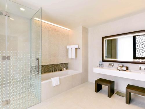 a bathroom with a glass shower and a sink at Alwadi Hotel Doha - MGallery Collection in Doha