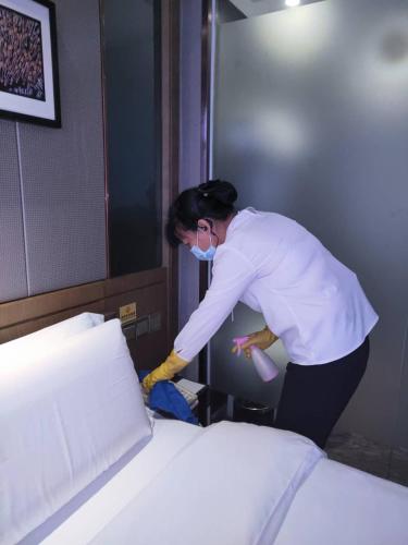 a woman is making a bed in a room at INSAIL Hotel (Shenzhen Dongmen Branch) in Shenzhen