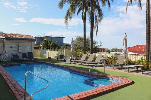 a large swimming pool with chairs and palm trees at Capri Apartments in Merimbula