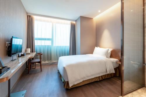 a hotel room with a bed and a desk and a television at Auto City Ruili Hotel in Jiading