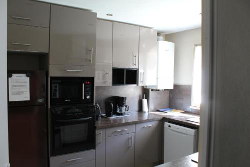 una cocina con electrodomésticos de acero inoxidable y armarios blancos en Maison du Lavoir Disneyland en Bailly-Romainvilliers