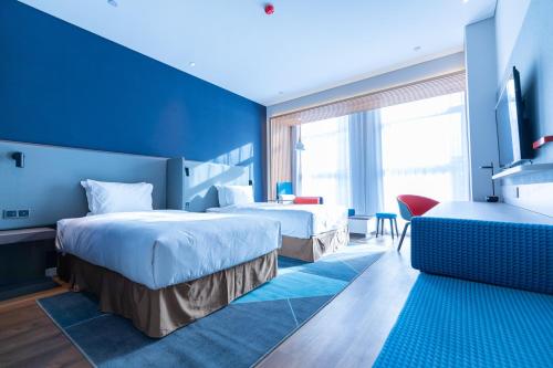 a hotel room with two beds and a blue wall at Holiday Inn Express Harbin Qunli by IHG in Harbin