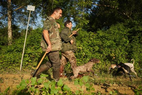 two men in military fatigues walking with their dogs at Castello di Bossi in Castelnuovo Berardenga