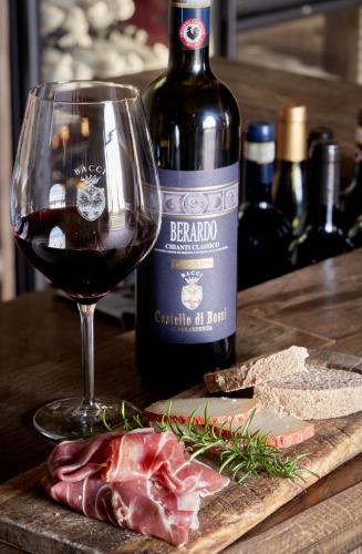 a glass of wine next to a bottle of wine and meat at Castello di Bossi in Castelnuovo Berardenga