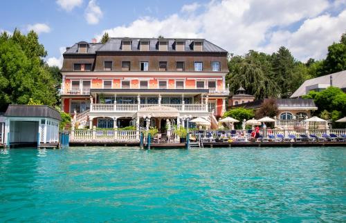 a large building on the water next to a body of water at Seehotel Porcia in Pörtschach am Wörthersee