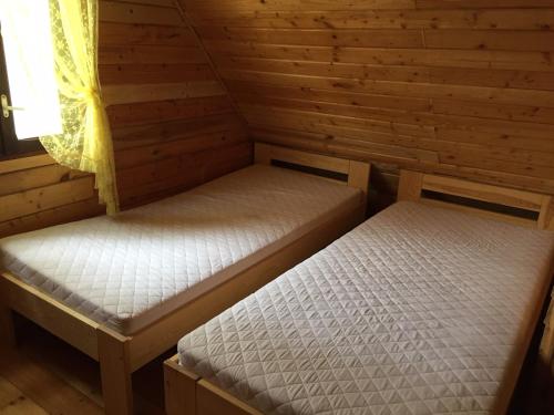 two beds in a wooden cabin with a window at Domek przy plaży in Narty