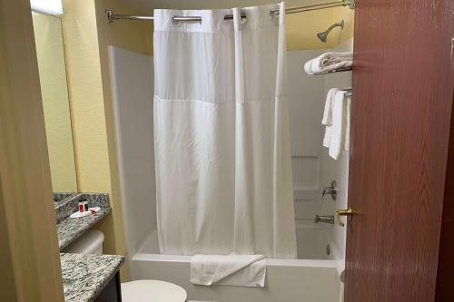a bathroom with a shower with a white shower curtain at Days Inn & Suites by Wyndham Tampa/Raymond James Stadium in Tampa