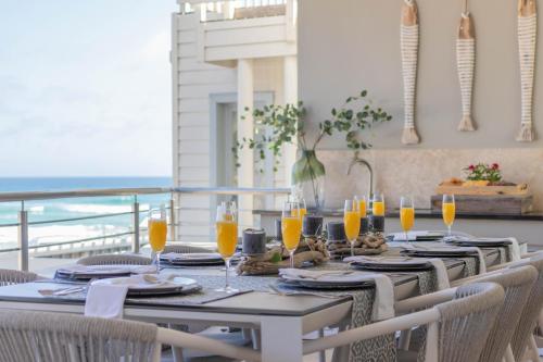 uma mesa de jantar com cadeiras e copos de sumo de laranja em Waves of Grace Seafront Villa em Herolds Bay