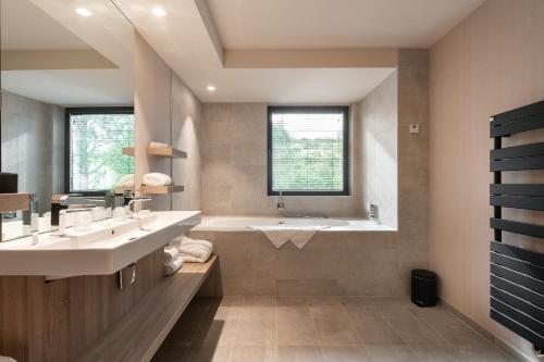 a bathroom with two sinks and a tub and a window at Hotel Restaurant Van Der Valk Nivelles-Sud in Nivelles