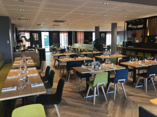 a restaurant with wooden tables and chairs in a room at Holiday Inn Bordeaux Sud - Pessac by IHG in Pessac