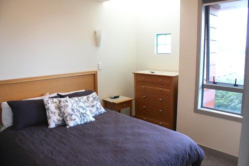 a bedroom with a bed and a dresser and a window at The Anchorage Apartments in Mount Maunganui
