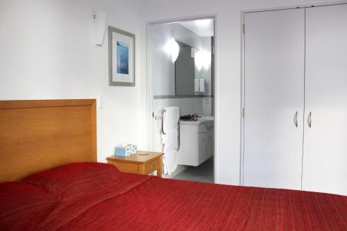a bedroom with a red bed and a bathroom at The Anchorage Apartments in Mount Maunganui