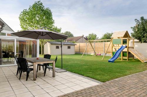 eine Terrasse mit einem Tisch mit einem Sonnenschirm und einem Spielplatz in der Unterkunft De Wilgoren in Kasterlee