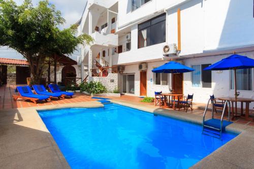 a swimming pool with blue chairs and umbrellas next to a building at Hotel La Casa de Judy in Puerto Ayora