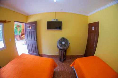 a yellow room with two beds and a fan at Euro Hostal in Guatemala