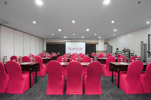 a conference room with red chairs and tables and a screen at favehotel Malang in Malang