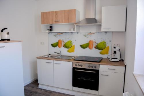 uma cozinha com armários brancos e frutas na parede em Ferienwohnung Landquartier em Schweppenhausen