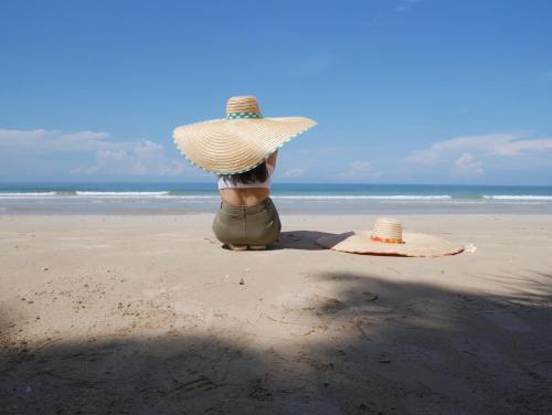 una persona seduta sulla spiaggia con un cappello di paglia di Baan Imm Sook Resort a Chao Lao Beach