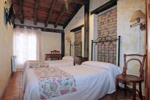 a bedroom with two beds and a chair and a window at HOTEL RURAL LOS ABUELOS in Montemayor de Pililla