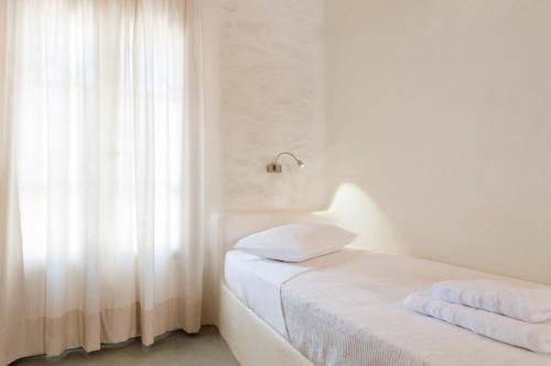 a white bedroom with a bed and a window at Yialos Ios Hotel in Ios Chora