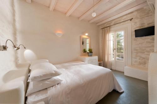 a white bedroom with a large bed and a window at Yialos Ios Hotel in Ios Chora