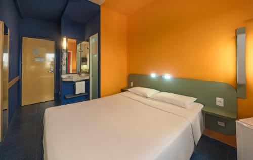 a bedroom with a large white bed with an orange wall at ibis budget Belem in Belém