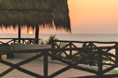 a sunset on the beach with a bench and a straw umbrella at Hotel Boutique La Puerta Azul Beachfront - Adults Only in Holbox Island