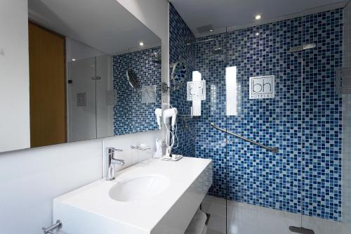 y baño con lavabo, espejo y azulejos azules. en Hotel bh Parque 93, en Bogotá