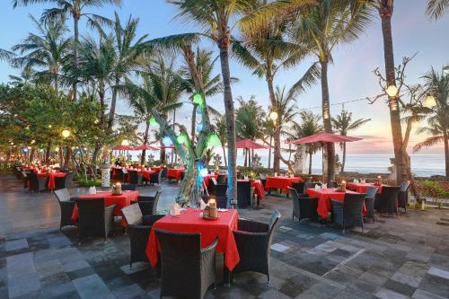 a restaurant with red tables and chairs and palm trees at Legian Beach Hotel in Legian