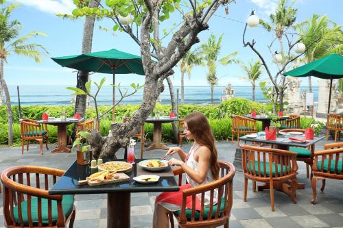 a woman sitting at a table eating food at a restaurant at Legian Beach Hotel in Legian