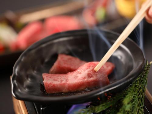 a piece of meat cooking in a pan with a chopstick at Hotel Tamanoyu in Matsumoto