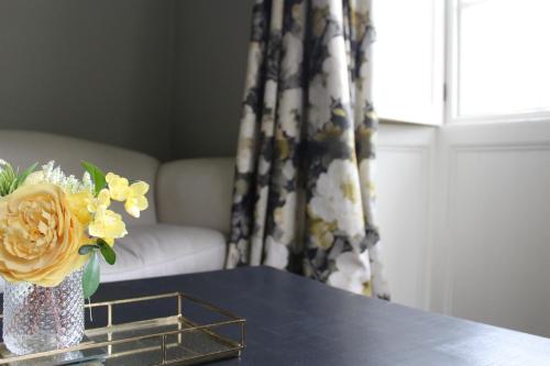 een tafel met een vaas met bloemen en een raam bij Dovenby Apartment- great base for exploring Lake District in Cockermouth