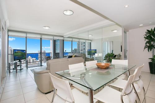 a dining room with a glass table and white chairs at Chevron Renaissance managed by Gchs in Gold Coast