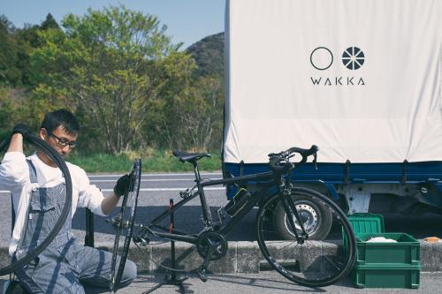 a man sitting next to a bike on the side of the road at WAKKA in Imabari