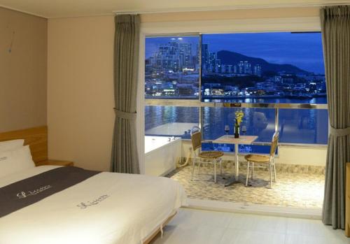 a bedroom with a large window and a table with chairs at Lium Spa Hostel in Yeosu