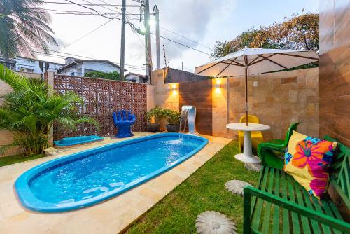 a swimming pool in a yard with a table and an umbrella at Águia Flats Pousada in Natal