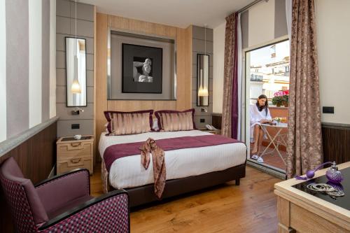 a hotel room with a bed and a woman sitting at a table at The Inn at the Spanish Steps Luxury Collection - Mario De' Fiori Suite in Rome