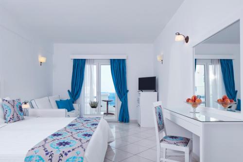 a hotel room with a bed, table, and window at Grand Beach Hotel in Mikonos