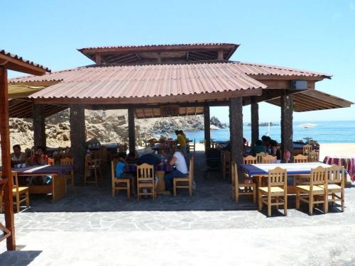 a group of people sitting at tables under a pavilion on the beach at Hotel Puerto Inka in Chala