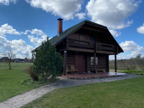 eine Blockhütte mit einer Veranda auf einem Feld in der Unterkunft Piešupīte in Staburags