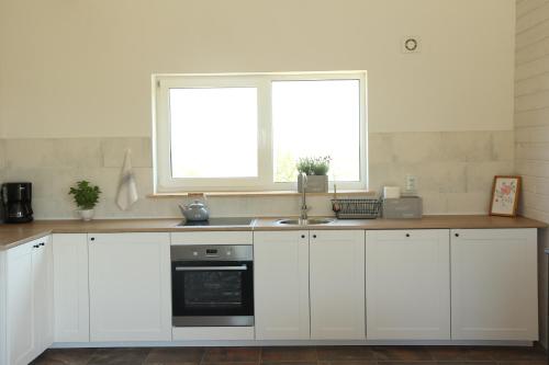 a kitchen with white cabinets and a sink and two windows at Mazury Garbate - Dom I przy Cisowym Jarze in Kowale Oleckie