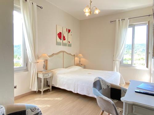 a bedroom with a bed and a desk and two windows at Hôtel Le Colombier in Moustiers-Sainte-Marie