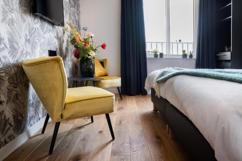 a bedroom with a yellow chair and a table with a vase of flowers at Boutique Hotel De Beerze in Middelbeers