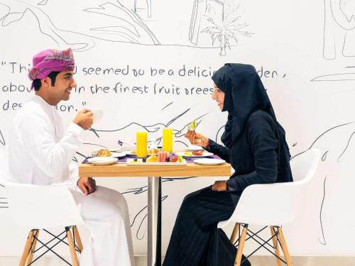 a man and a woman sitting at a table eating food at Mercure Sohar in Sohar